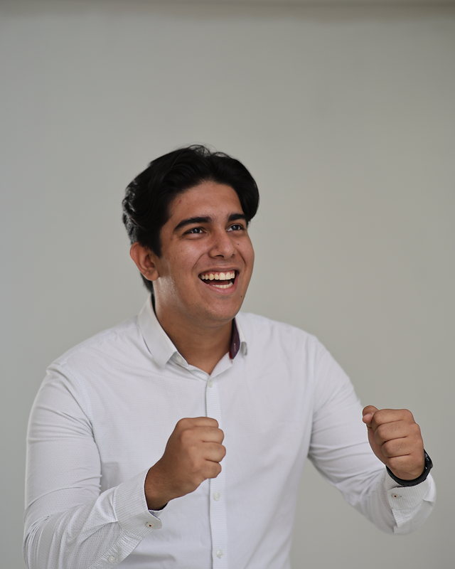 Victor Carvalho de camisa branca, punhos erguidos, comemorando e sorrindo.